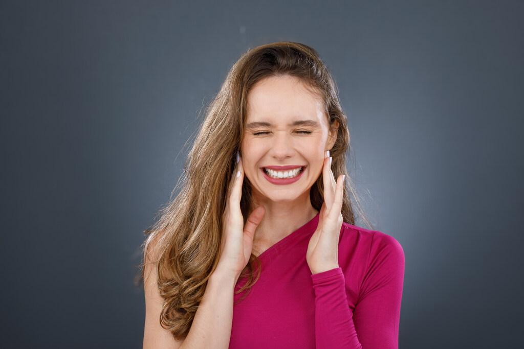 Mulher demonstrando desconforto causado por sensibilidade nos dentes, com expressão de dor e mãos próximas ao rosto.