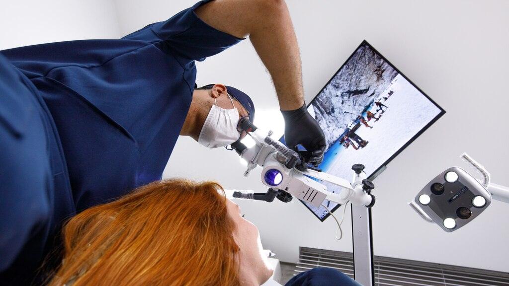 Dentista realiza procedimento com microscópio e tecnologia avançada durante cirurgia para colocação de implante dentário.